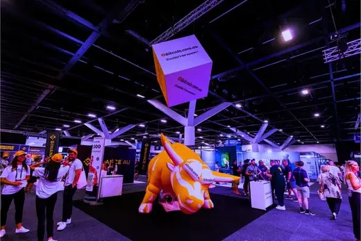 The AusCryptoCon expo floor with a large inflatable bull and exhibitor stands.