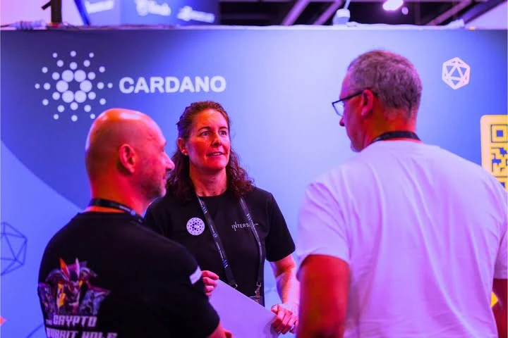Three attendees talking in front of the Cardano stand.